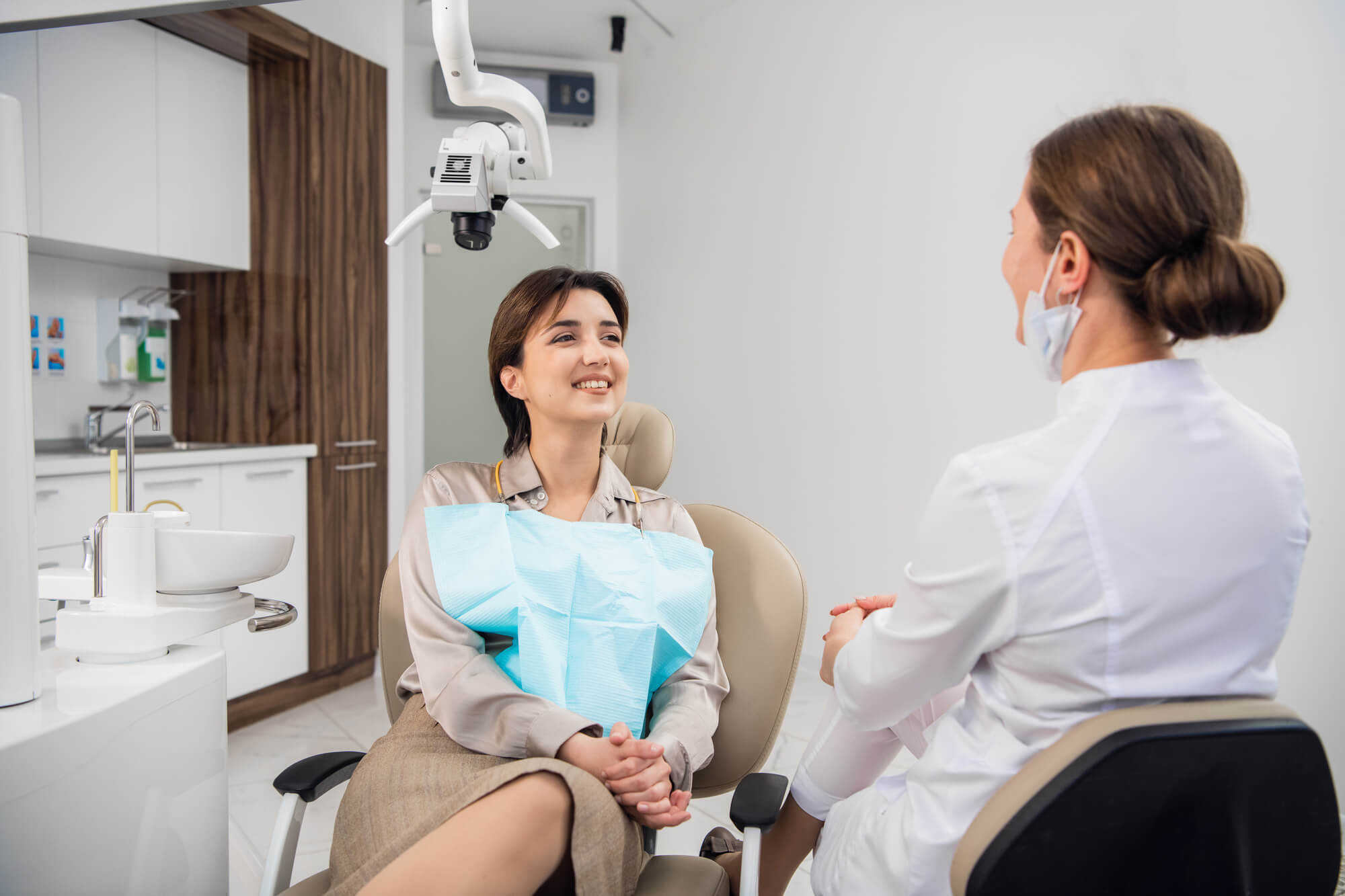 A woman at the dentists office chatting to her doctor and smiling with a toothy smile